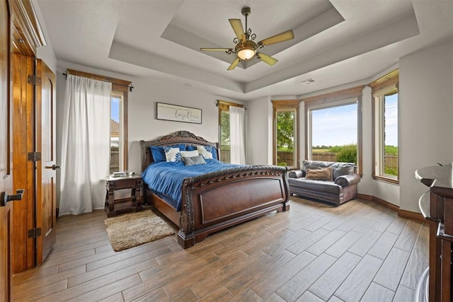 bedroom with ceiling fan, a tray ceiling, and multiple windows