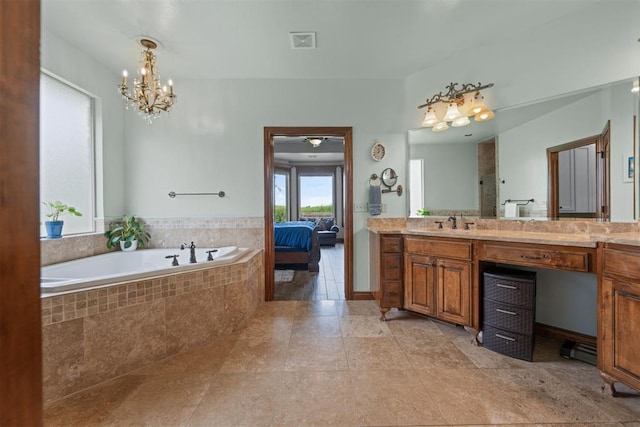 bathroom with tiled tub, vanity, tile patterned floors, and a chandelier