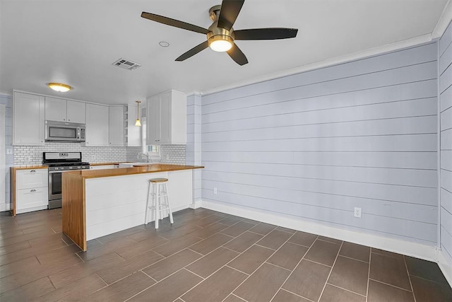 kitchen with a breakfast bar, wooden counters, appliances with stainless steel finishes, kitchen peninsula, and white cabinets