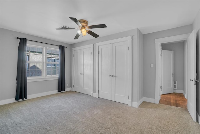 unfurnished bedroom featuring light carpet, multiple closets, and ceiling fan