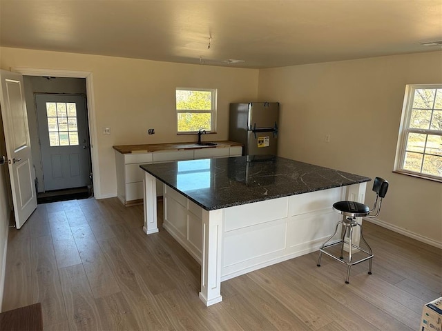 kitchen with white cabinetry, a wealth of natural light, a kitchen island, and stainless steel refrigerator