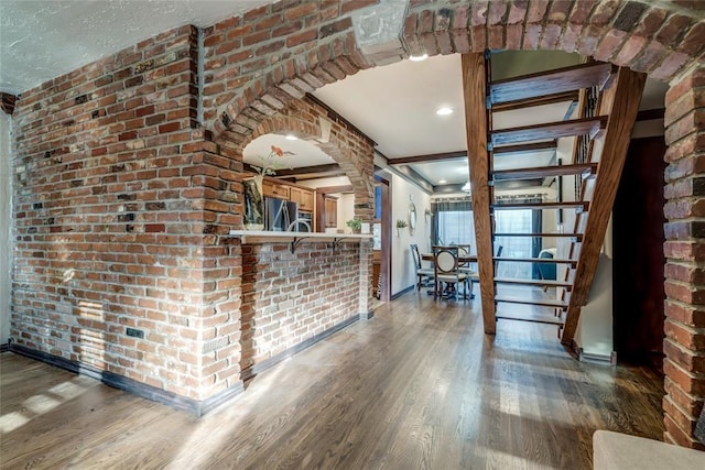 unfurnished living room with dark wood-type flooring and brick wall