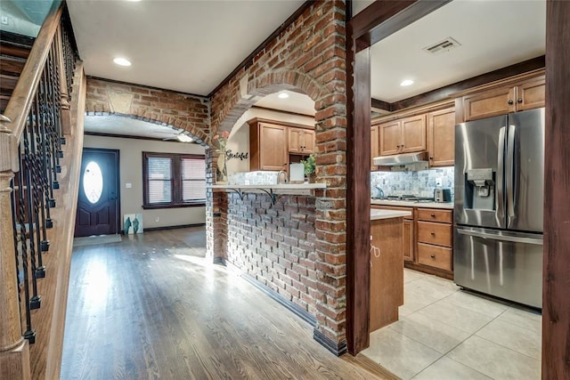 kitchen featuring tasteful backsplash, stainless steel fridge, light hardwood / wood-style floors, and brick wall