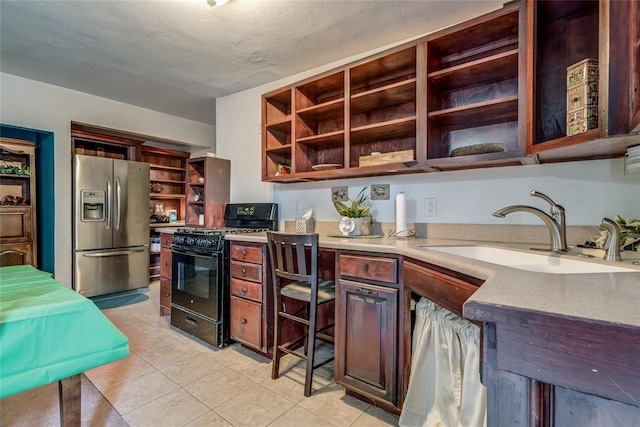 kitchen featuring sink, stainless steel fridge with ice dispenser, a textured ceiling, light tile patterned floors, and black gas range oven