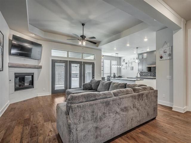 living room featuring a raised ceiling, ceiling fan, dark hardwood / wood-style floors, and a fireplace