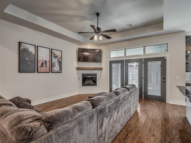 living room featuring dark wood-type flooring, ceiling fan, and a raised ceiling