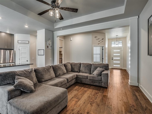 living room with a tray ceiling, ceiling fan with notable chandelier, and dark hardwood / wood-style floors