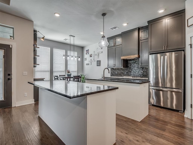 kitchen featuring wall chimney range hood, stainless steel refrigerator, backsplash, a kitchen island, and decorative light fixtures