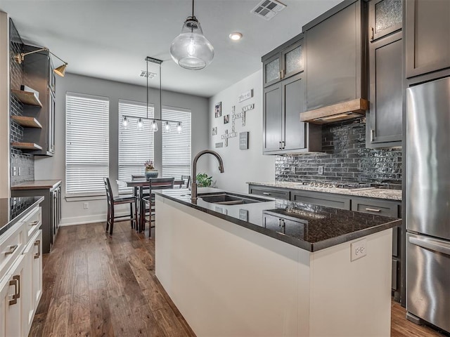 kitchen featuring decorative light fixtures, white cabinetry, sink, stainless steel appliances, and a center island with sink