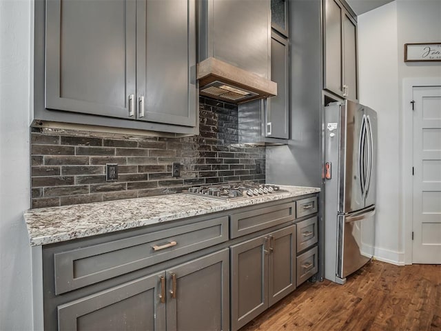 kitchen with light stone counters, gray cabinets, stainless steel appliances, and custom range hood