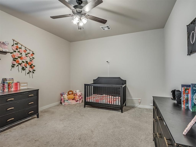 bedroom with a nursery area, light carpet, and ceiling fan