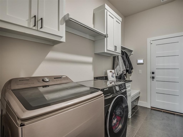 laundry area featuring dark tile patterned flooring, washing machine and dryer, and cabinets