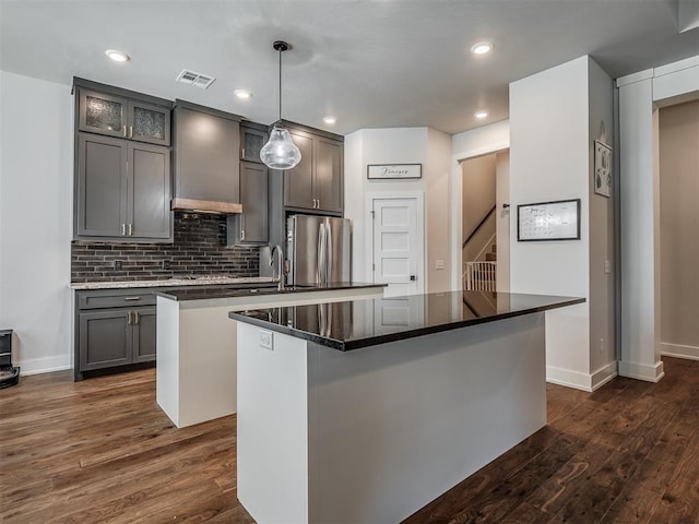 kitchen with visible vents, an island with sink, dark wood-style flooring, freestanding refrigerator, and a sink