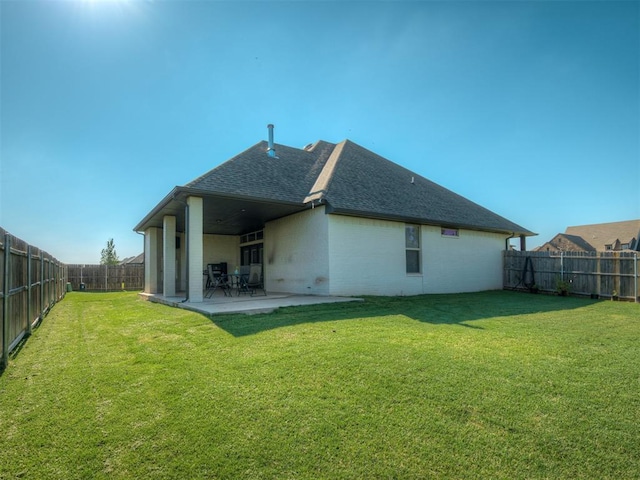 back of house with a patio, a fenced backyard, a lawn, and roof with shingles