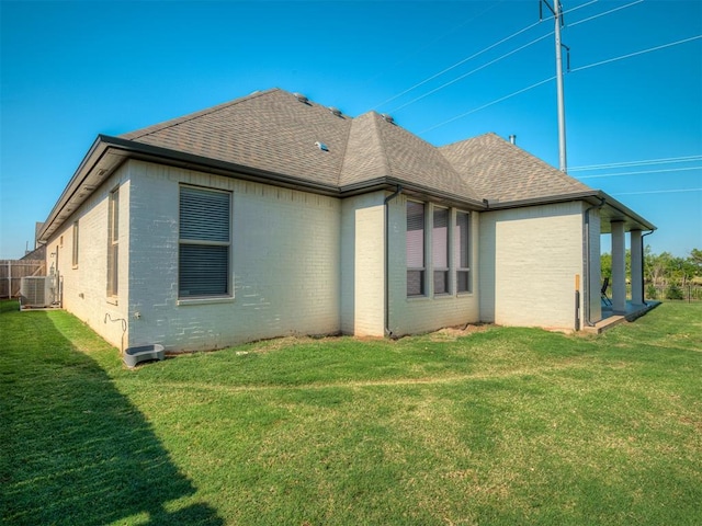 back of house featuring brick siding, roof with shingles, and a lawn