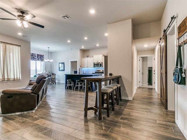 dining room with a barn door and ceiling fan with notable chandelier