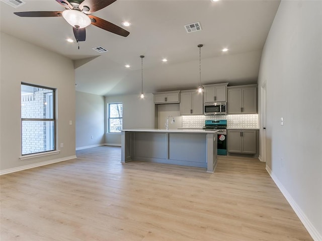 kitchen with vaulted ceiling, a center island with sink, appliances with stainless steel finishes, gray cabinets, and backsplash