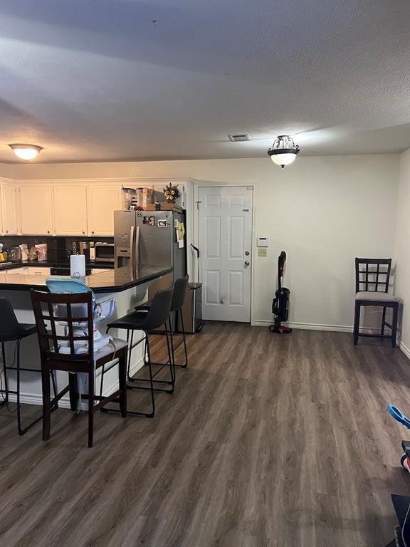 kitchen with a breakfast bar, white cabinetry, backsplash, stainless steel refrigerator with ice dispenser, and dark wood-type flooring