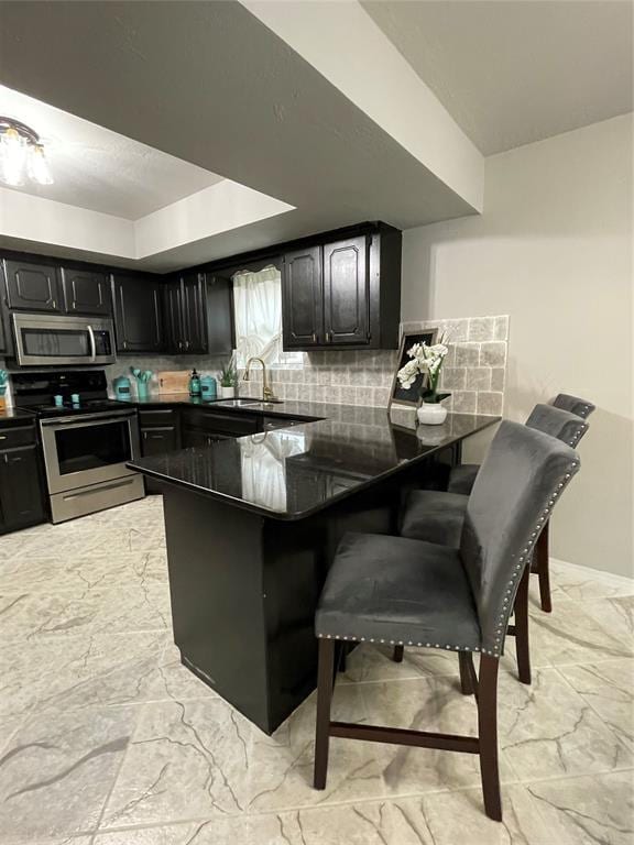 kitchen featuring sink, stainless steel appliances, tasteful backsplash, a kitchen bar, and kitchen peninsula