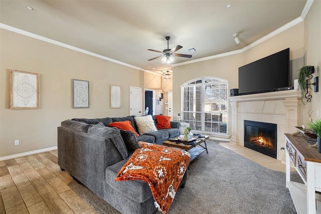 living room featuring crown molding, ceiling fan, light hardwood / wood-style floors, and a tile fireplace