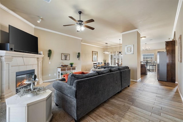 living room with crown molding, ceiling fan with notable chandelier, a tile fireplace, and light wood-type flooring