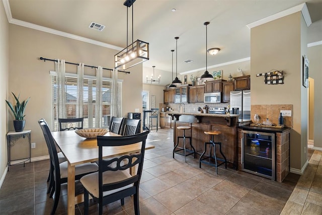 dining space with wine cooler, crown molding, tile patterned flooring, and an inviting chandelier