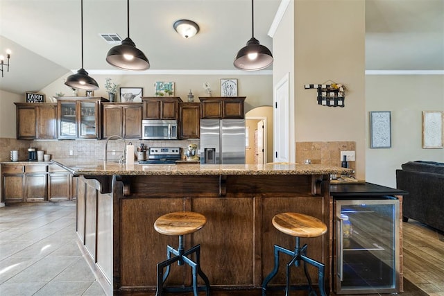 kitchen featuring light stone counters, a breakfast bar area, stainless steel appliances, and beverage cooler