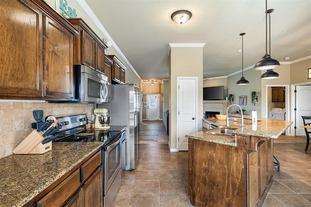 kitchen with sink, crown molding, appliances with stainless steel finishes, an island with sink, and backsplash