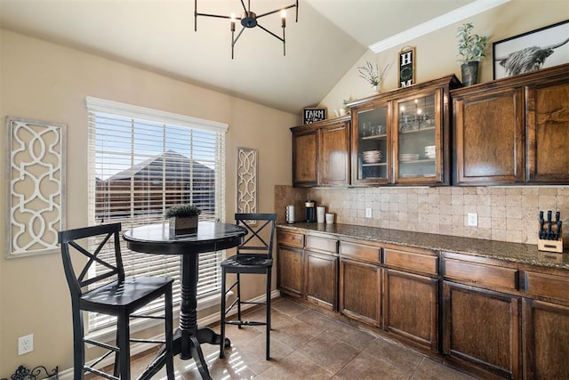 kitchen with vaulted ceiling, dark tile patterned flooring, dark stone counters, decorative backsplash, and dark brown cabinetry