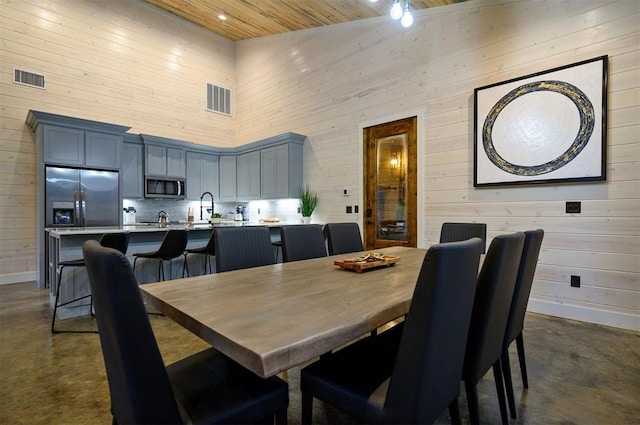 dining space featuring wood ceiling, wooden walls, sink, and a high ceiling