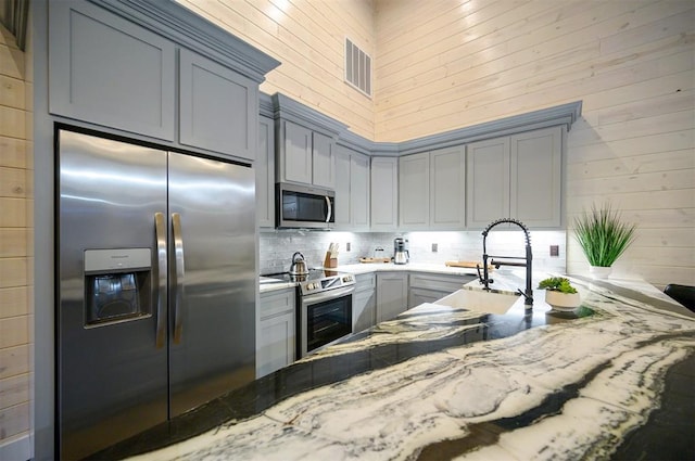 kitchen with sink, gray cabinetry, light stone counters, appliances with stainless steel finishes, and decorative backsplash