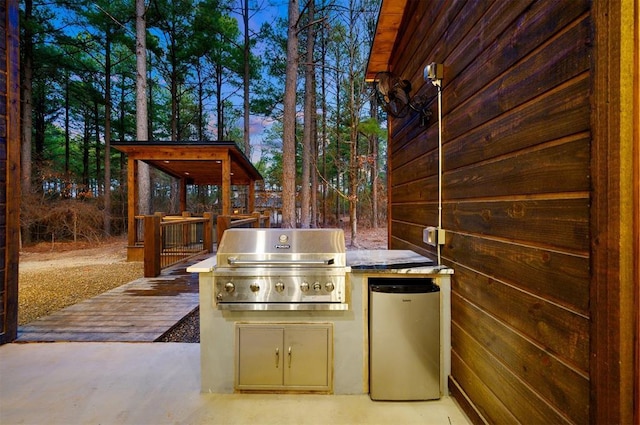 patio terrace at dusk with exterior kitchen, a grill, and a deck