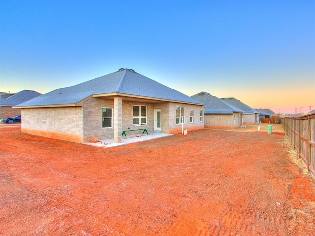 rear view of property featuring roof with shingles, brick siding, fence, and a patio