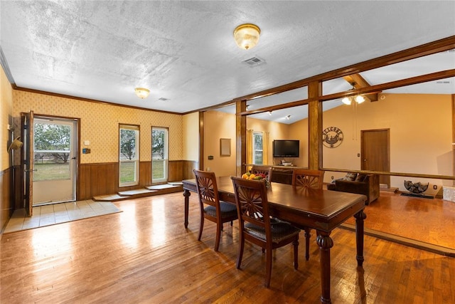 dining area featuring ornamental molding, vaulted ceiling, a wainscoted wall, visible vents, and wood-type flooring
