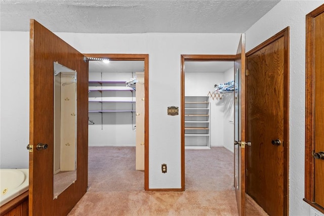 hall with light carpet, baseboards, and a textured ceiling
