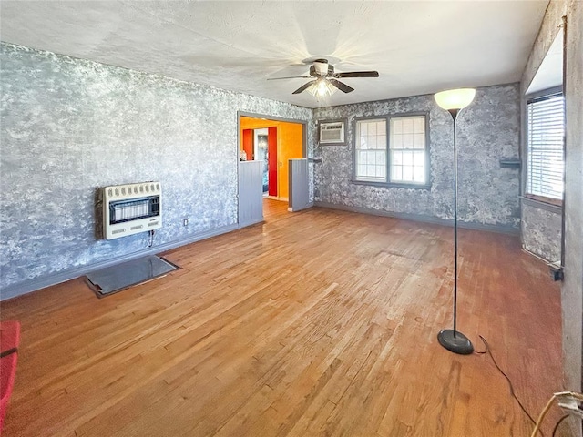 unfurnished living room with heating unit, a wealth of natural light, wood finished floors, and an AC wall unit