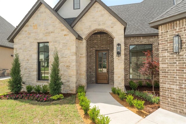 doorway to property with brick siding, roof with shingles, and stone siding