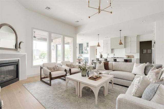 living area featuring a chandelier, a glass covered fireplace, light wood-style flooring, and visible vents