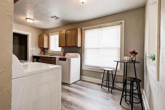 laundry room with sink, washing machine and dryer, a textured ceiling, and light wood-type flooring