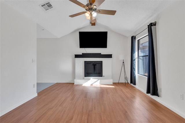 unfurnished living room featuring lofted ceiling, ceiling fan, a fireplace, wood-type flooring, and a textured ceiling