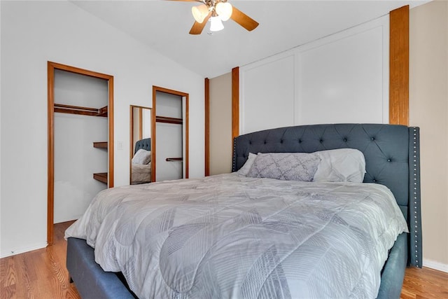 bedroom featuring multiple closets, vaulted ceiling, ceiling fan, and light wood-type flooring