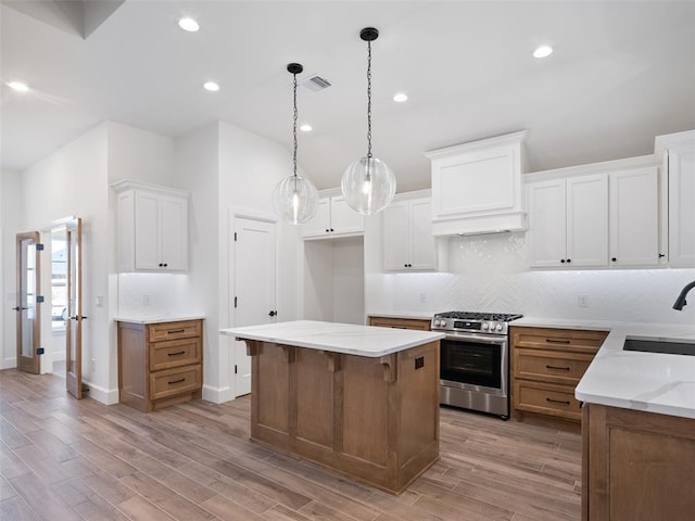 kitchen with sink, premium range hood, stainless steel range with gas stovetop, a center island, and white cabinets