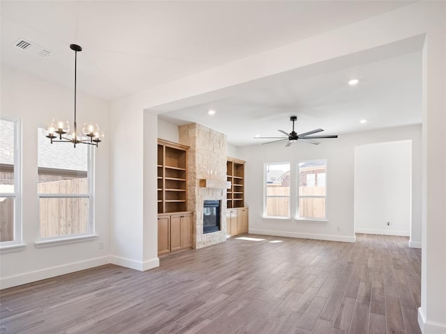 unfurnished living room with light wood-type flooring, ceiling fan with notable chandelier, and a fireplace