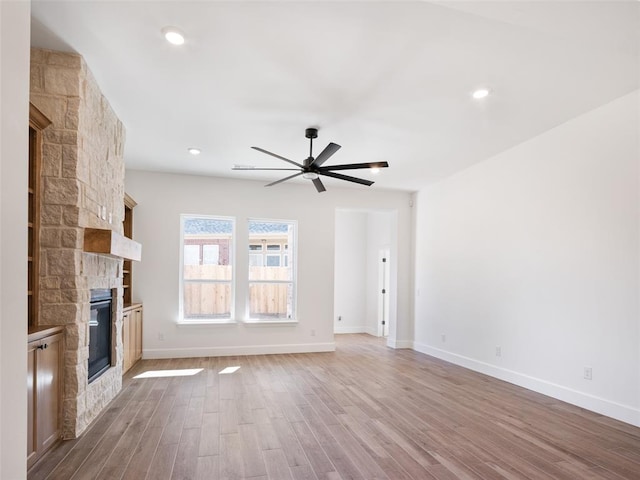 unfurnished living room with ceiling fan, a stone fireplace, and light wood-type flooring