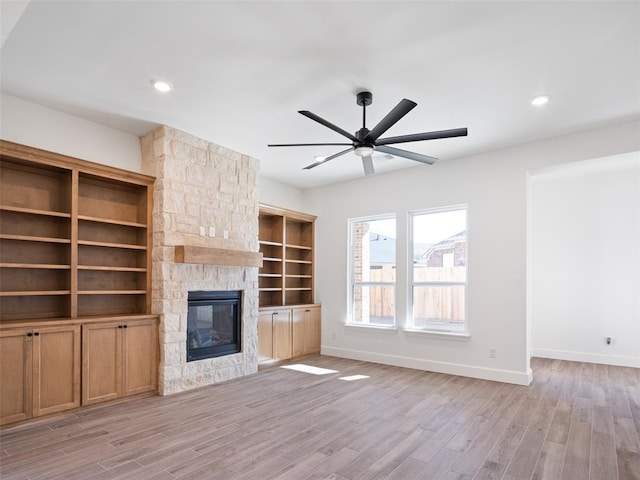 unfurnished living room featuring ceiling fan, a stone fireplace, and light hardwood / wood-style flooring