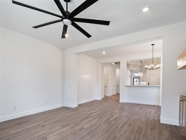 unfurnished living room featuring ceiling fan with notable chandelier and light wood-type flooring