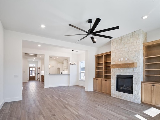 unfurnished living room with a stone fireplace, ceiling fan with notable chandelier, and light hardwood / wood-style flooring