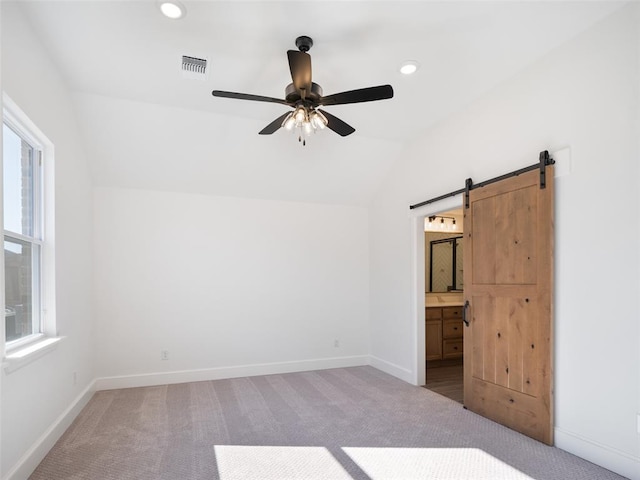 carpeted spare room featuring a barn door, a wealth of natural light, lofted ceiling, and ceiling fan