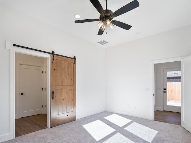 unfurnished bedroom with a barn door, light colored carpet, and ceiling fan