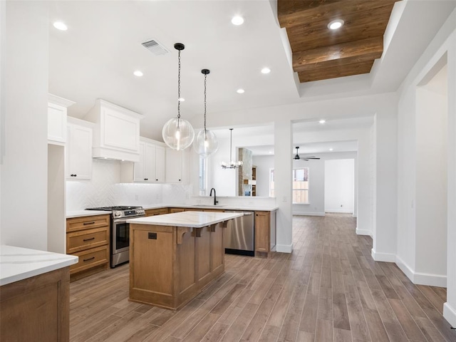 kitchen with sink, custom exhaust hood, a center island, stainless steel appliances, and white cabinets